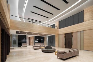 A spacious lobby with a high ceiling, modern lighting, and a central seating area with sofas and a coffee table. - Hotel Neo Plus Airport Jakarta (Tangerang)