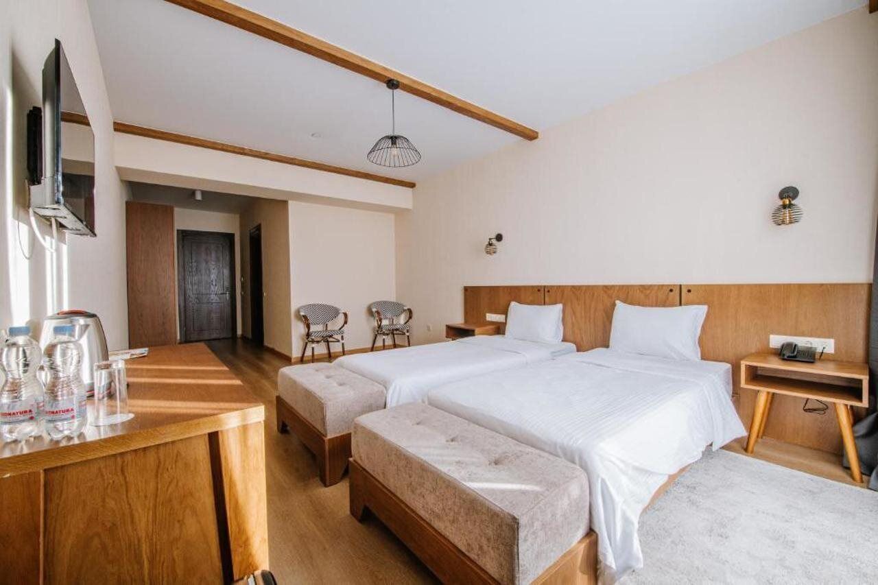 A hotel room with two beds, a wooden desk with a mirror, a small table, and two chairs.