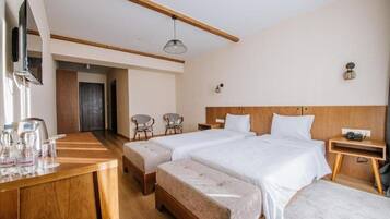 A hotel room with two beds, a wooden desk with a mirror, a small table, and two chairs.