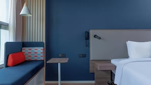 A hotel room with a blue wall, a bed with white bedding, a small table, a blue sofa with a red pillow, and a hanging light fixture. - Holiday Inn Express Shenzhen Guangming Cloud Park (Shenzhen)