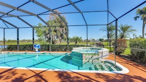 A covered swimming pool with a hot tub, surrounded by a fence and palm trees. - Pool, Spa & Lanai: Upscale Retreat in Fort Myers! (Fort Myers)