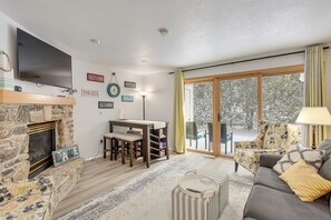 A cozy living room with a stone fireplace, a flat-screen TV, a dining table with chairs, a sofa with cushions, and a large window with curtains. - Charming DC Getaway Steps from D’town Fish Creek (Fish Creek)