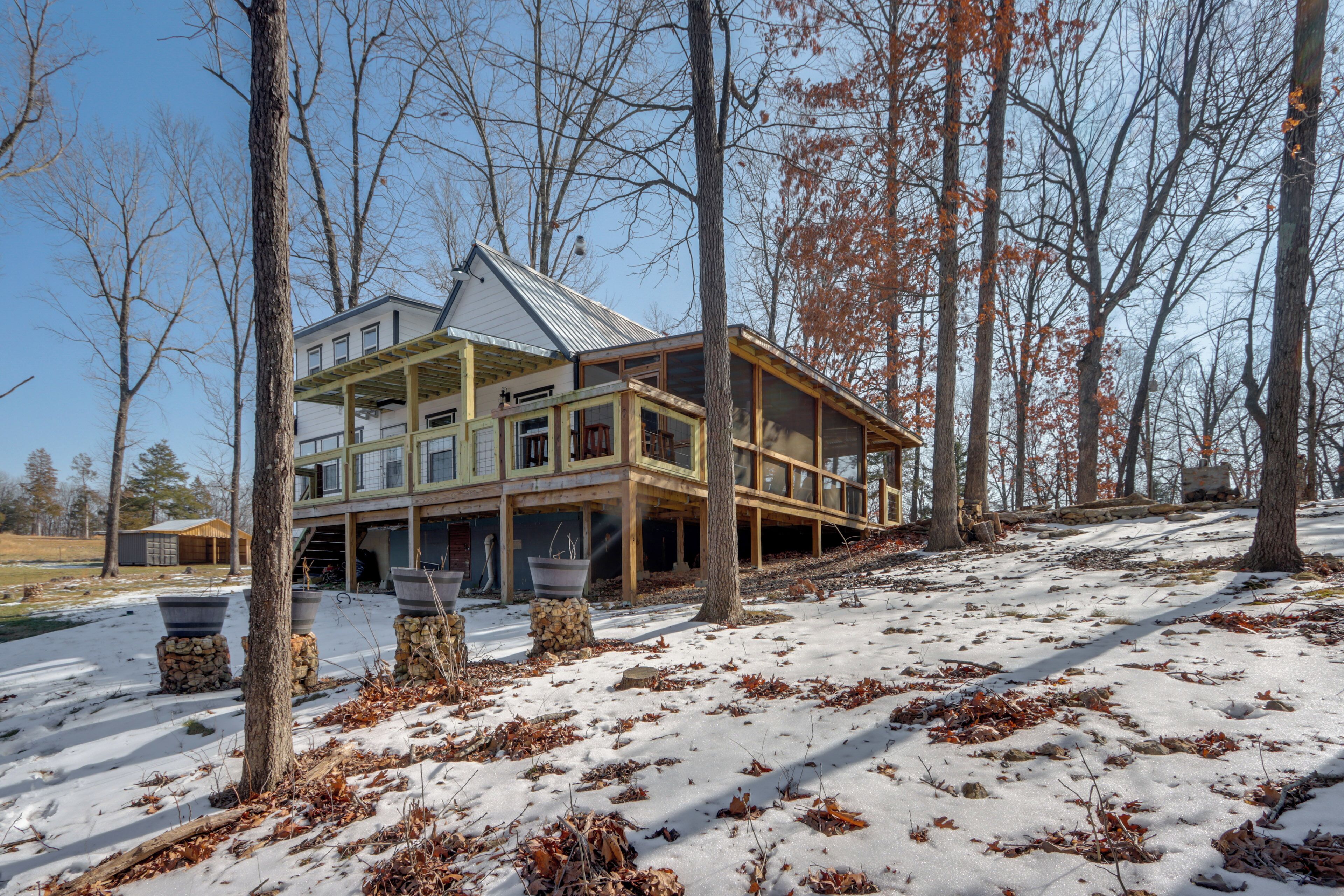Une grande maison à plusieurs étages, dotée d’une terrasse en bois et d’un toit en métal, entourée d’arbres et recouverte de neige.