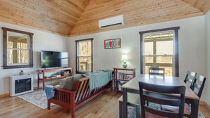 Un accogliente soggiorno con soffitto in legno, una televisione, un camino, un tavolo da pranzo con sedie e ampie finestre.
