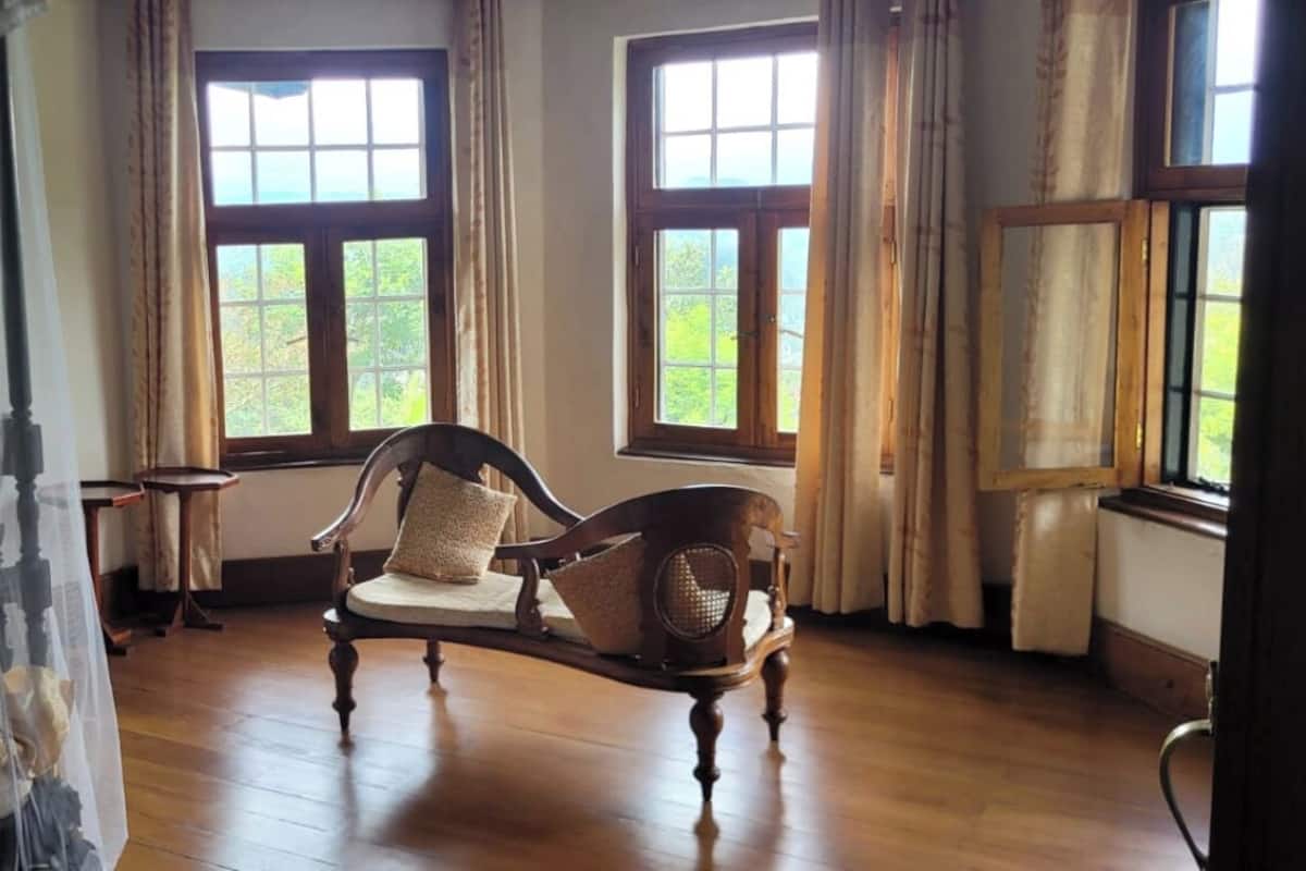 Ein Zimmer mit einem Bett, das mit einem transparenten Vorhang drapiert ist, einem Holzstuhl mit Kissen und einem Fenster mit Blick auf Grünflächen.