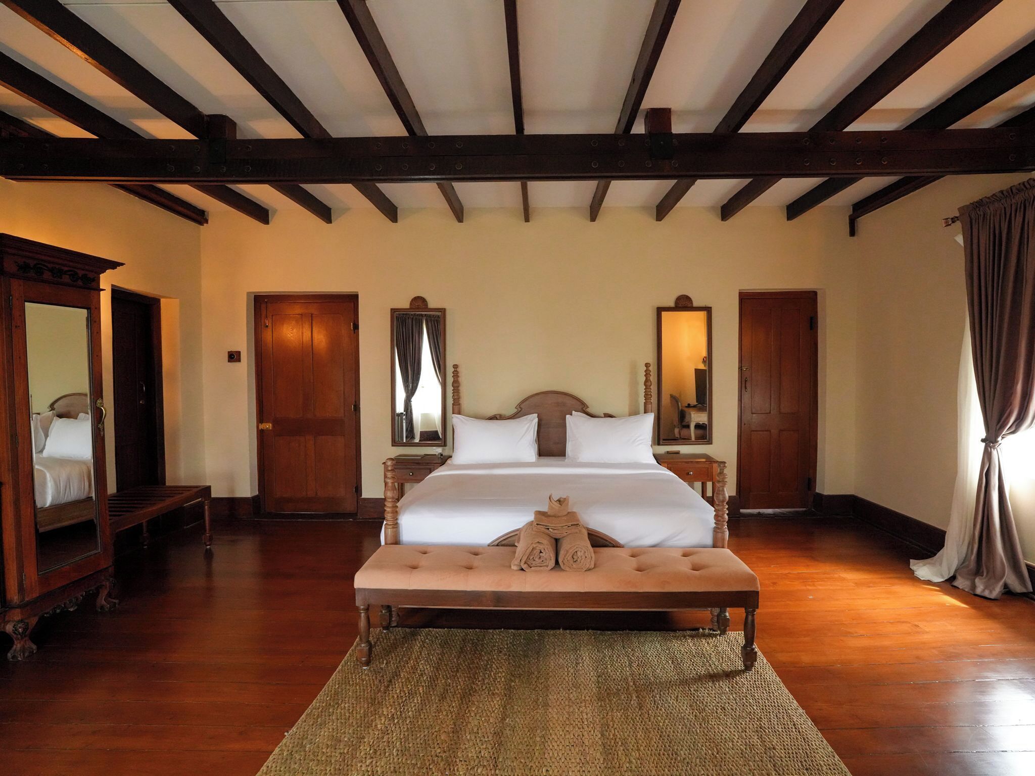 Una habitación de hotel con una cama grande, suelo de madera y techo de madera con vigas a la vista.