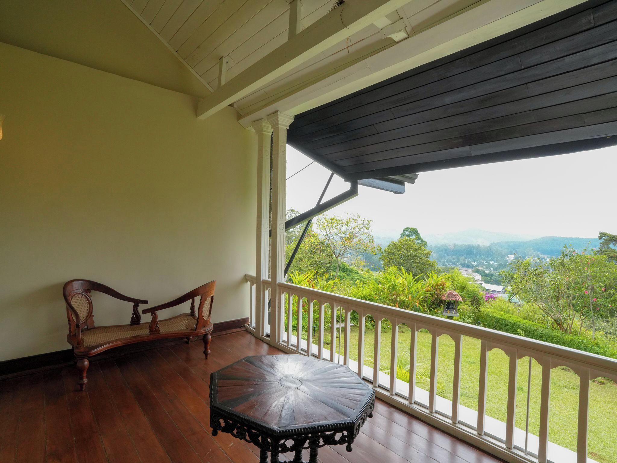 A balcony with a wooden table and two chairs, overlooking a lush green landscape with distant hills.