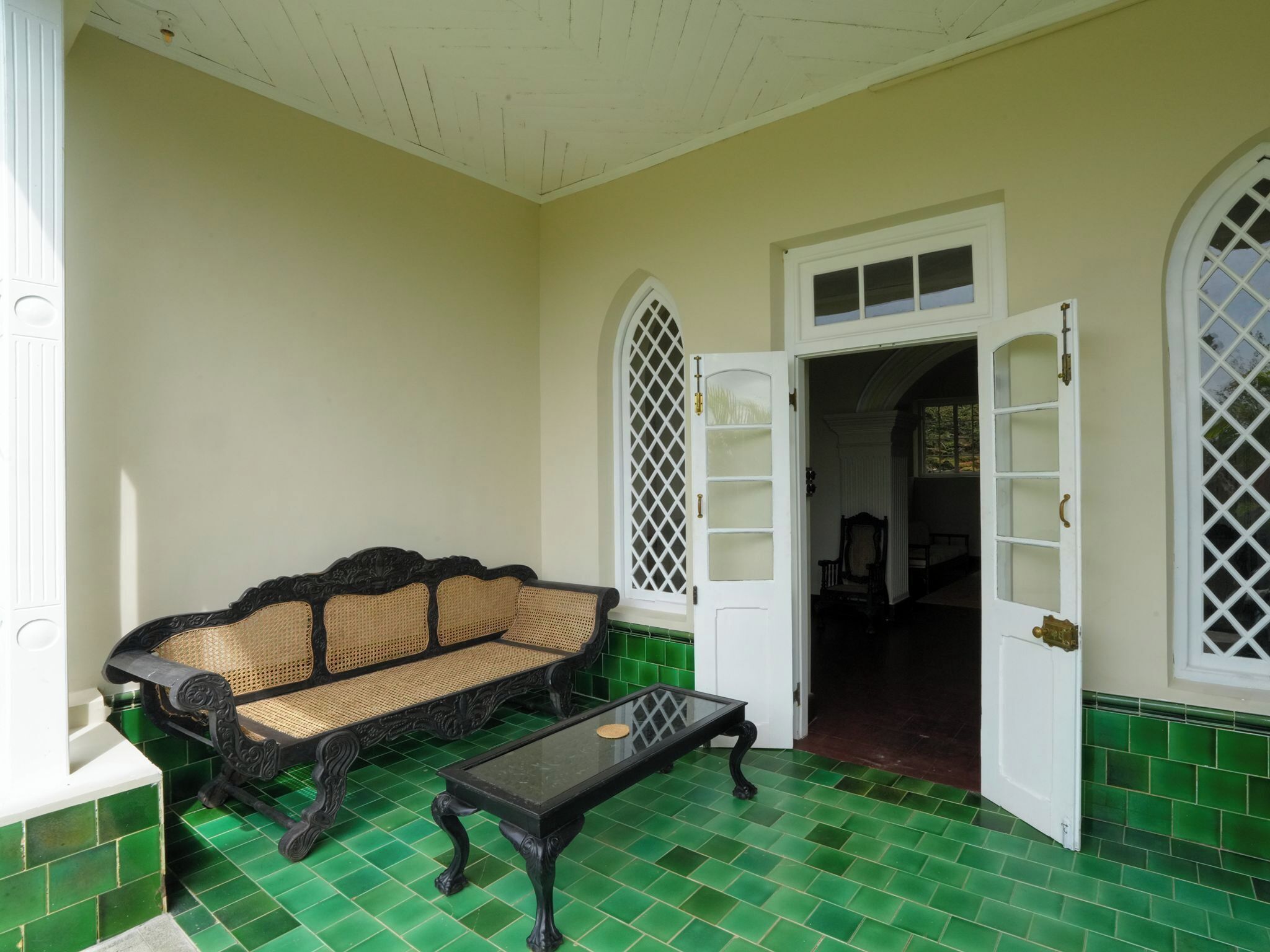 Una habitación con piso de baldosas verdes, un sofá negro con asiento tejido y una mesa a juego.