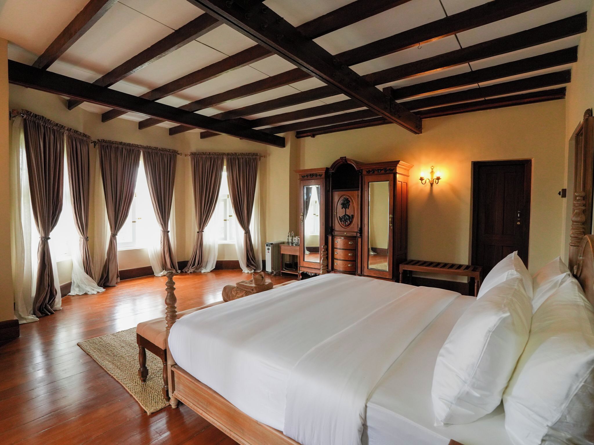 A hotel room with a large bed, wooden floor, and a ceiling with exposed beams.