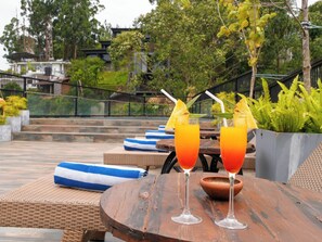 Two glasses of orange beverage on a wooden table with a view of a garden and buildings in the background. - Graystone Bungalow by Seven Angels (Diyatalawa)