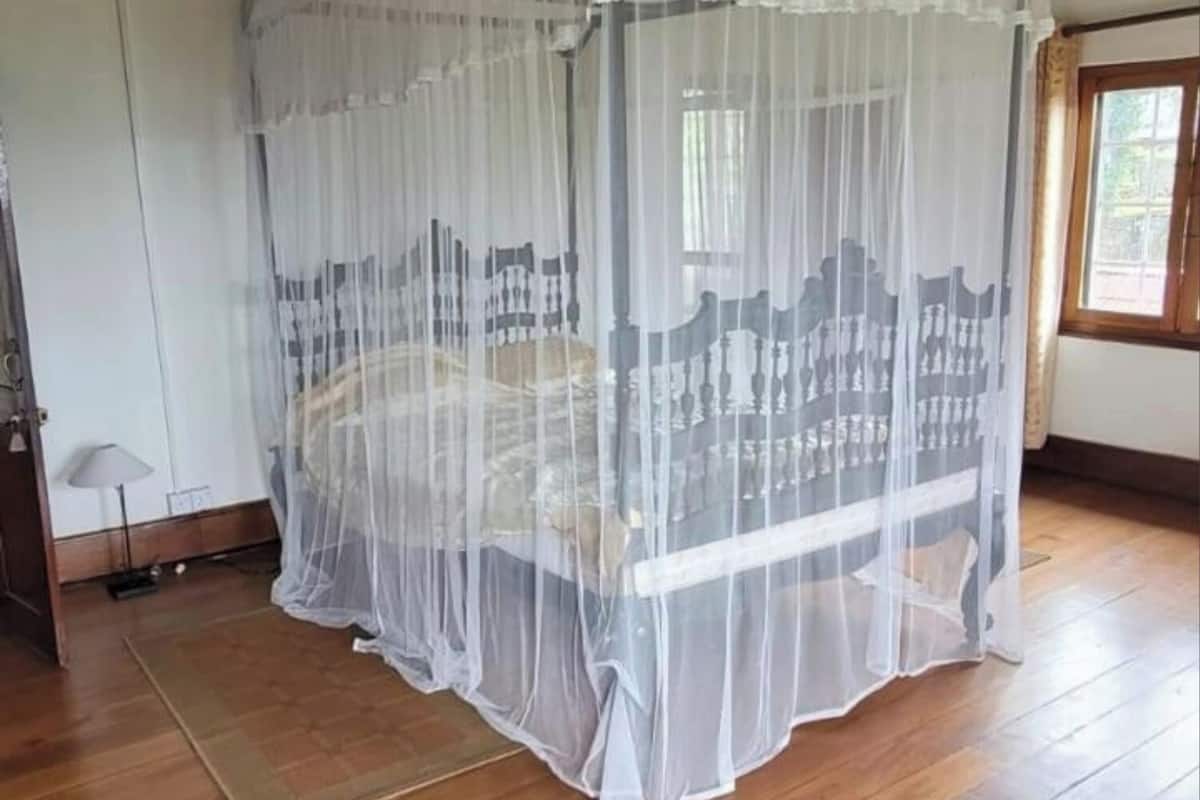Ein Zimmer mit einem Bett unter einem weißen Baldachin, Holzbalken an der Decke, einem Fenster und einer Lampe.