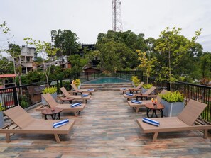 A rooftop lounge area with lounge chairs and tables, a swimming pool, and surrounding greenery. - Graystone Bungalow by Seven Angels (Diyatalawa)