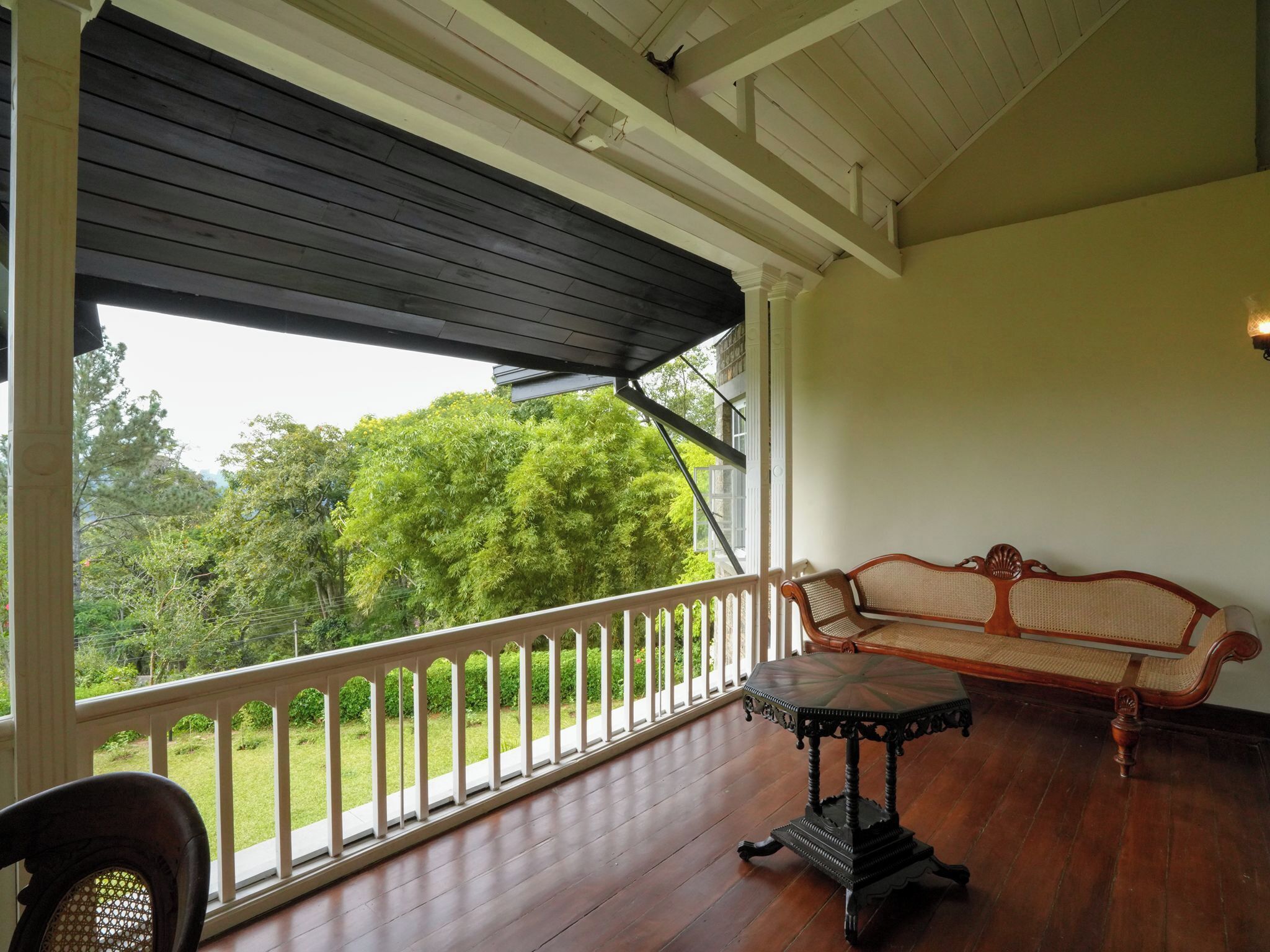 Varanda coberta com mesa de madeira e sofá, com vista para uma paisagem verde exuberante.