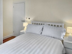 A neatly made bed with white linens, a white headboard, and two bedside lamps on matching nightstands.