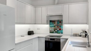 Eine moderne Küche mit weißen Schränken, einem eingebauten Ofen, einer Spülmaschine und einer farbenfrohen Spritzschutzwand.