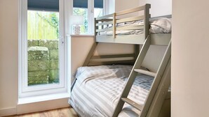 Ein Stockbett in einem Zimmer mit Fenster, Holzboden und Blick auf einen Garten.
