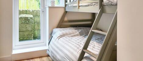 Una cama en literas en una habitación con ventana, suelo de madera y vistas a un jardín.