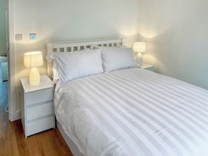 Una cama bien hecha con ropa de cama a rayas, dos lámparas de noche y una mesita de noche blanca con cajones.