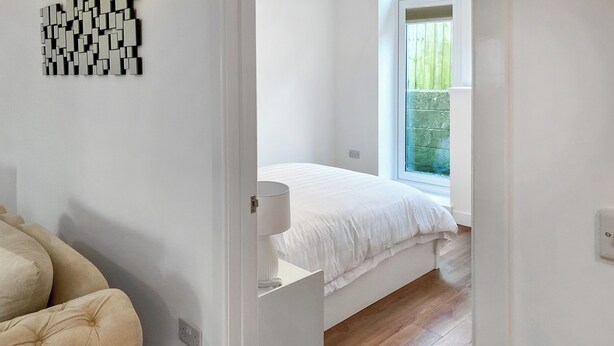Ein Schlafzimmer mit Bett, Nachttisch, Sessel und Fenster.