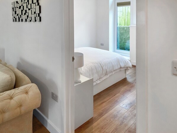 Un dormitorio con cama, mesita de noche, silla y ventana.