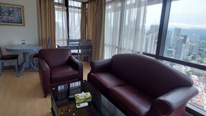 Una sala moderna con sofá de cuero, una mesa de centro de vidrio y un comedor con mesa y sillas. Amplias ventanas ofrecen vista a la ciudad.