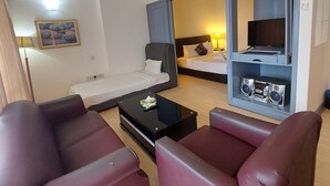 Una habitación de hotel con cama, escritorio con computadora, televisión y dos sillones.