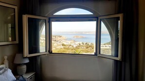 A room with a large arched window offering a view of a coastal town and the sea. - Family 5BR Villa with sea views, private pool, summer kitchen & spacious garden (Almyrida)