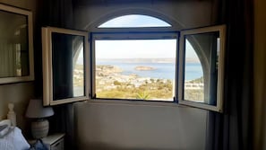 Ein Zimmer mit einem großen Bogenfenster, das Blick auf eine Küstenstadt und das Meer gewährt.
