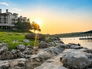 Une vue sur le fleuve, avec un coucher de soleil, un terrain rocheux et un bâtiment doté de balcons.