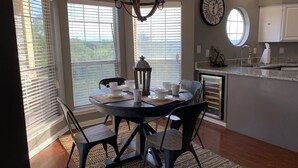 A dining area with a round table, chairs, a chandelier, and a view through large windows. - Relaxing Lago Vista Hill Country Loft w/ Free Parking & Deer Sightings (Lago Vista)