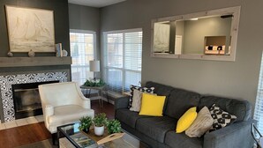 A living room with a fireplace, a grey sofa with yellow pillows, a white armchair, and a coffee table with magazines. - Relaxing Lago Vista Hill Country Loft w/ Free Parking & Deer Sightings (Lago Vista)
