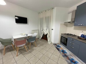 Una cucina compatta con angolo pranzo, una TV montata a parete e una tenda che copre la finestra.