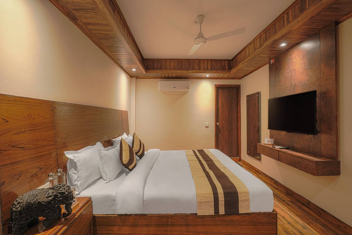 A hotel room with a wooden headboard, a bed with white and brown bedding, a flat-screen TV mounted on the wall, and an air conditioning unit.