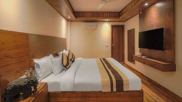 Ein Hotelzimmer mit hölzernem Kopfteil, einem Bett mit weißer und brauner Bettwäsche, einem flachbildfernseher an der Wand und einer Klimaanlage.