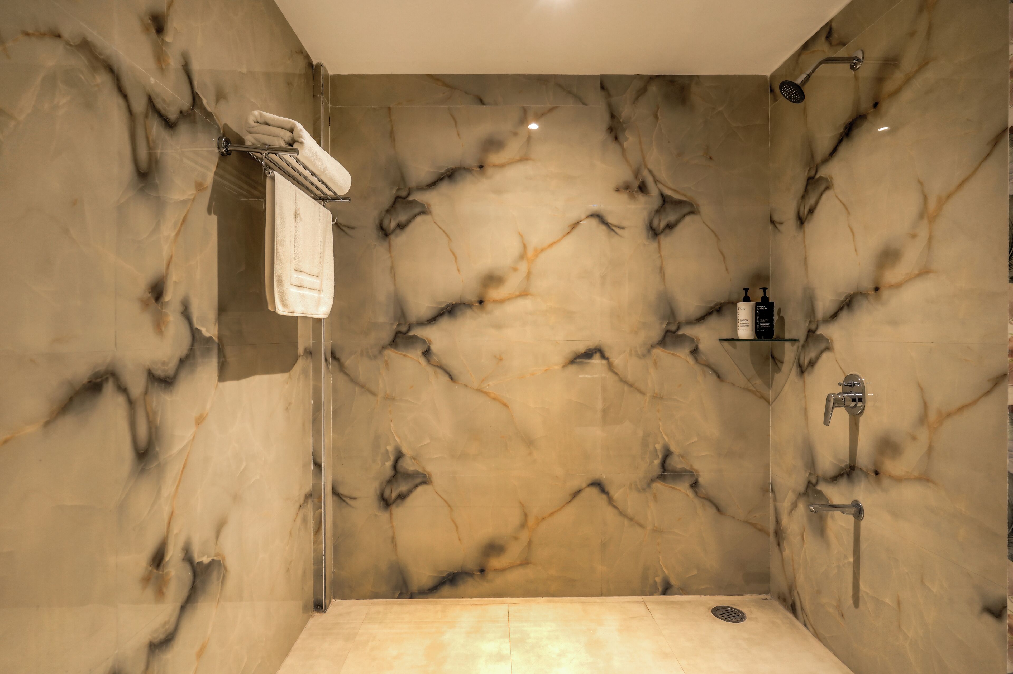 A marble-walled shower with a towel rack, a shelf with toiletries, and a handheld showerhead.