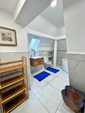 A modern bathroom with a marble floor, a wooden shelf unit, a blue bath mat, and a wicker basket.