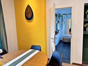 A dining area with a round table, chairs, a clock on the wall, and a view into a room with a door.