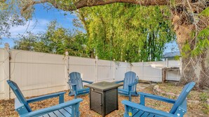 Eine Terrasse mit blauen Adirondack-Stühlen, einem kleinen Tisch und einem weißen Zaun.