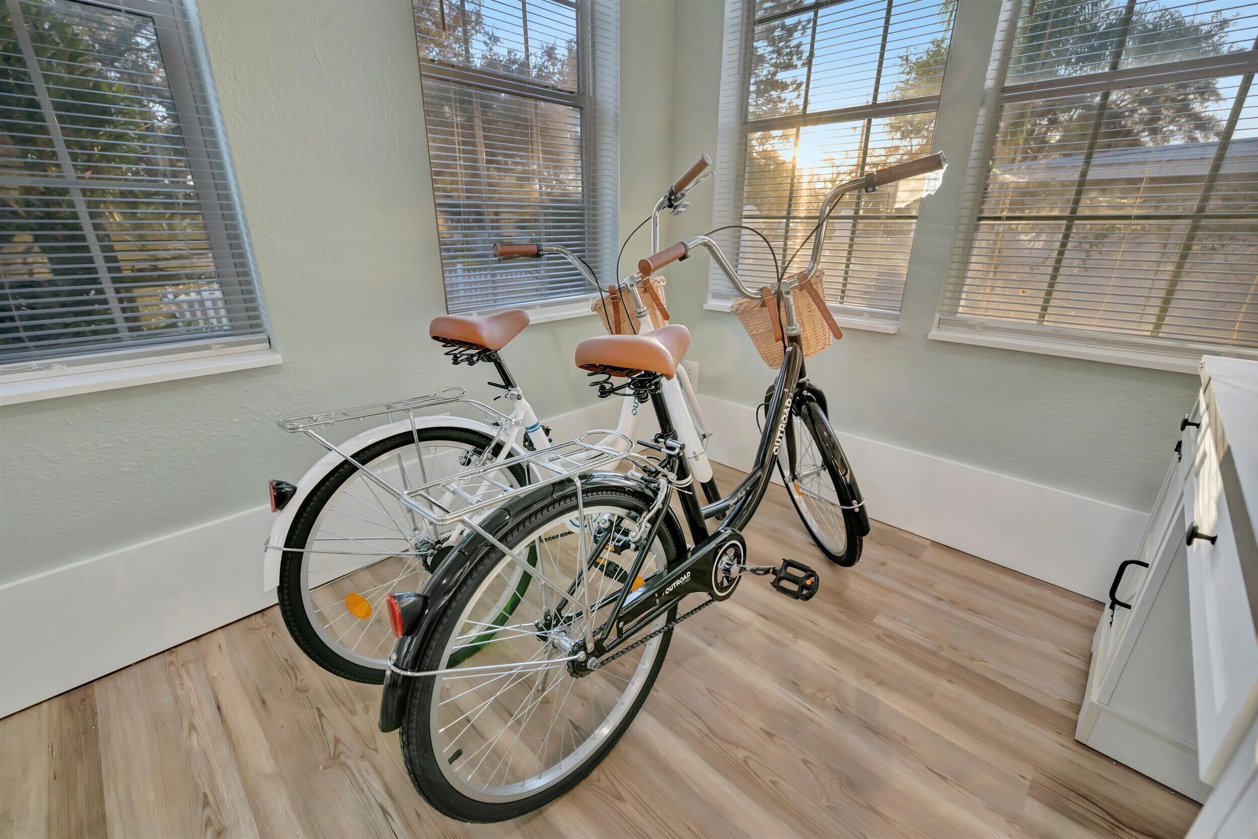 Una habitación con dos bicicletas, un armario blanco y ventanas grandes con persianas.