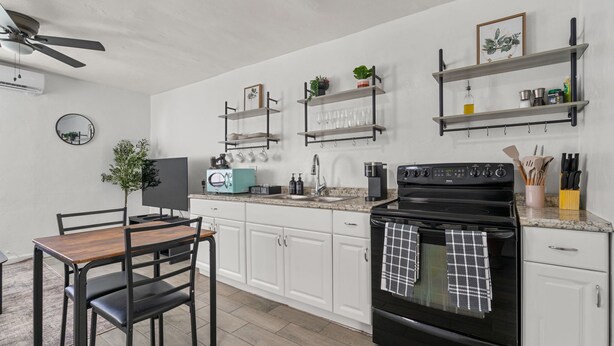 A modern kitchen with white cabinets, a black stove, and a dining area with a wooden table and chairs. - Casa Esmeralda · Cozy · Midtown Gem (Tucson)