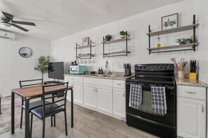 A modern kitchen with white cabinets, a black stove, and a dining area with a wooden table and chairs. - Casa Esmeralda · Cozy · Midtown Gem (Tucson)