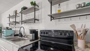 A kitchen with a stove, sink, and shelves with kitchenware. - Casa Esmeralda · Cozy · Midtown Gem (Tucson)