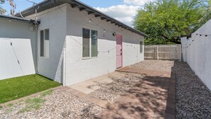 A white building with a red door, a small lawn, and a wooden fence. - Casa Esmeralda · Cozy · Midtown Gem (Tucson)
