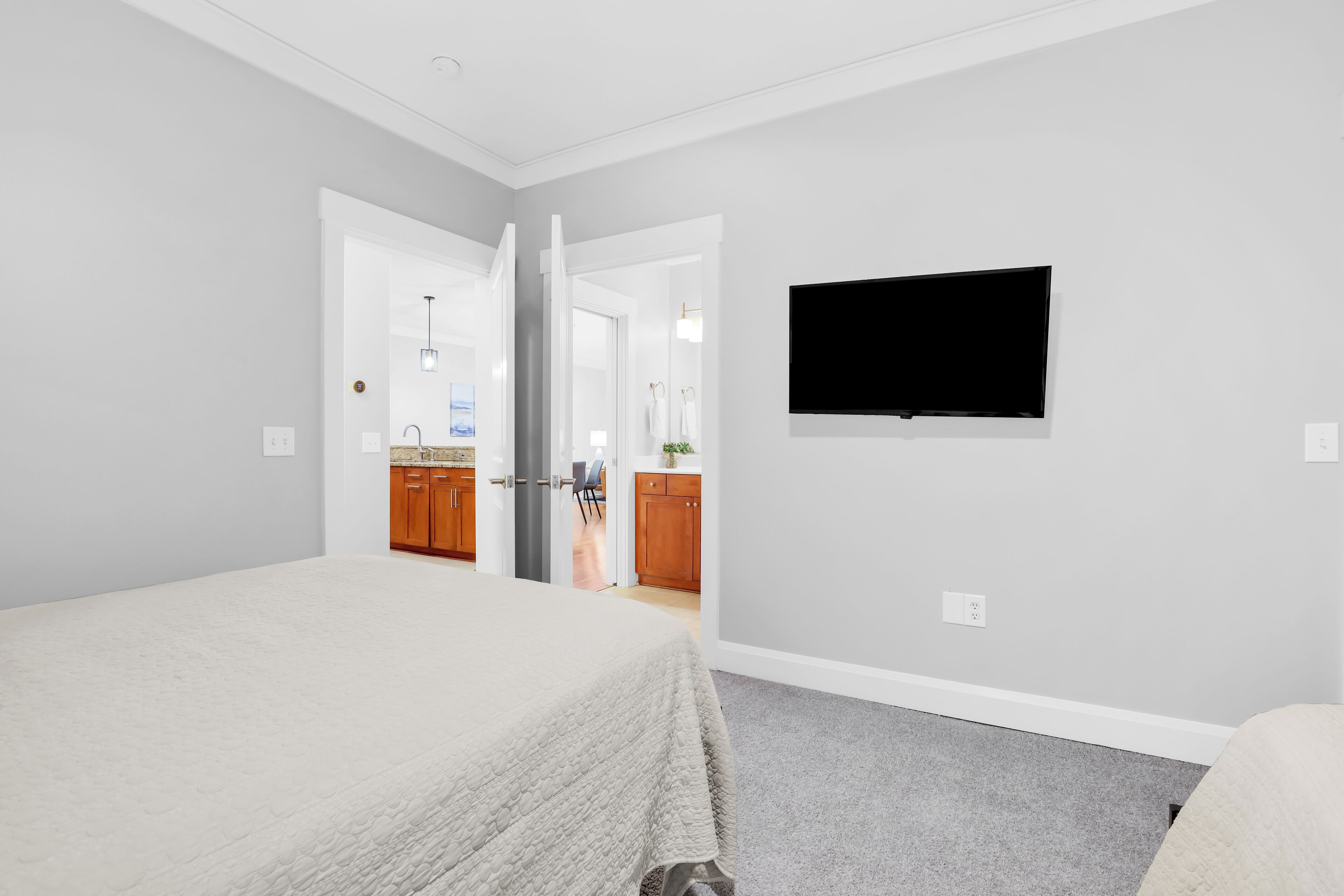 Ein Schlafzimmer mit einem Bett, einem an der Wand montierten Fernseher und Blick in das angrenzende Badezimmer.