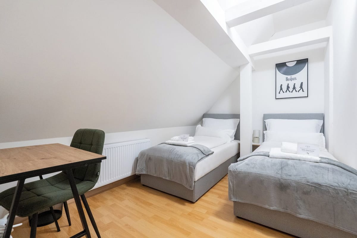 A small, modern room with two single beds, a wooden table, and a chair.