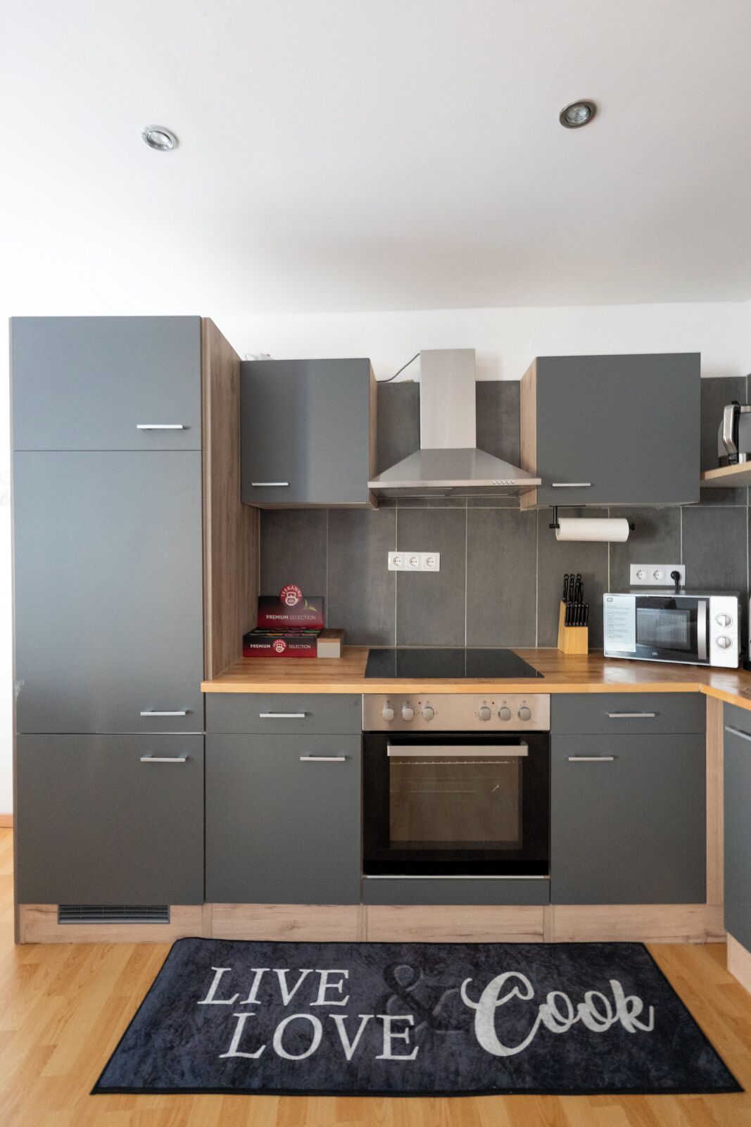 Eine moderne Küche mit grauen Schränken, einem Herd, einem Backofen, einer Mikrowelle und einer Holz Arbeitsplatte.