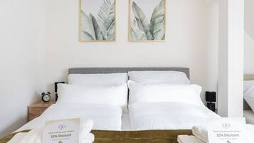 A hotel room with a double bed, two framed botanical prints on the wall, a bedside table with a lamp, and a sign offering a 10% discount on direct bookings.