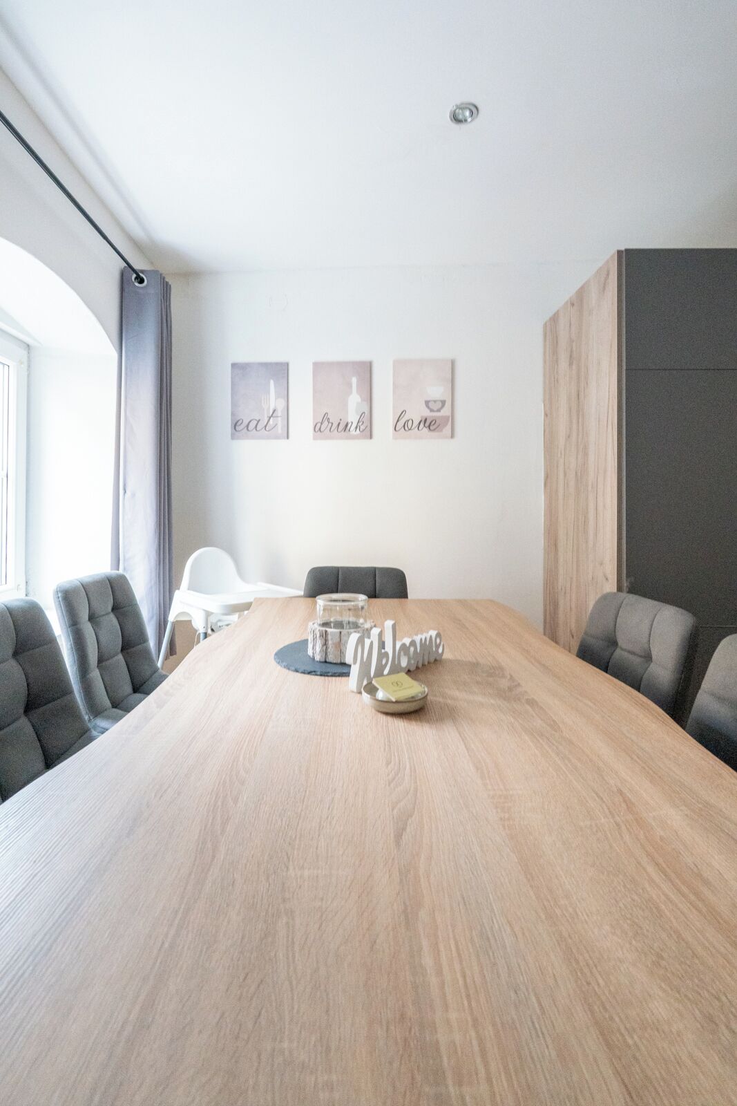 A conference room with a wooden table, grey upholstered chairs, and three framed wall art pieces with words 'eat', 'drink', and 'love'.