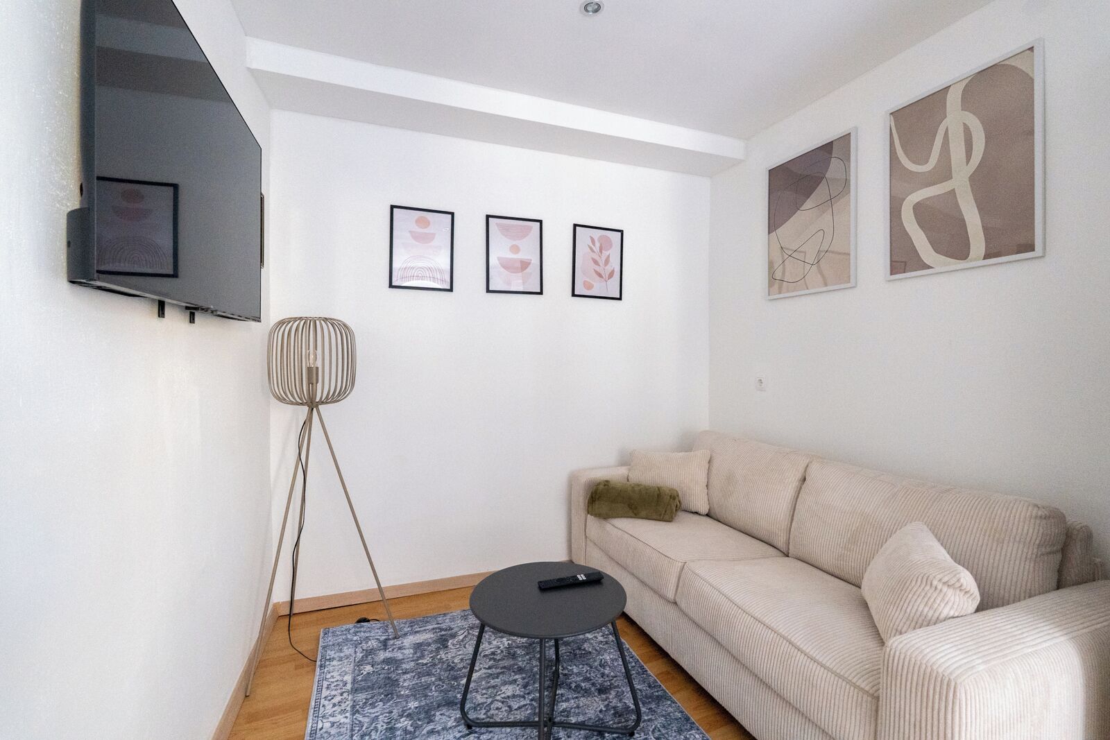 A modern living room with a beige sofa, a floor lamp, a coffee table, and three framed artworks on the wall.