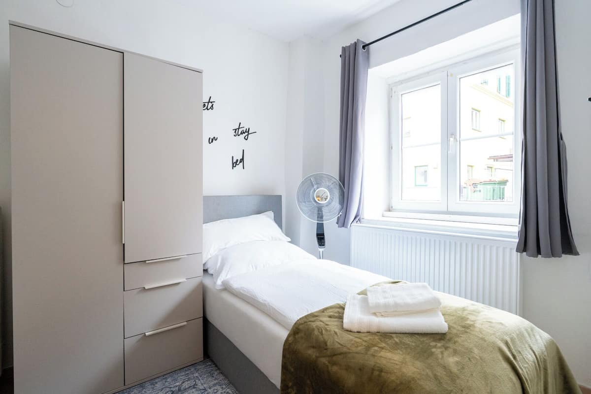 A bedroom with a bed, a wardrobe, a radiator, a window with curtains, and a wall with a motivational quote.